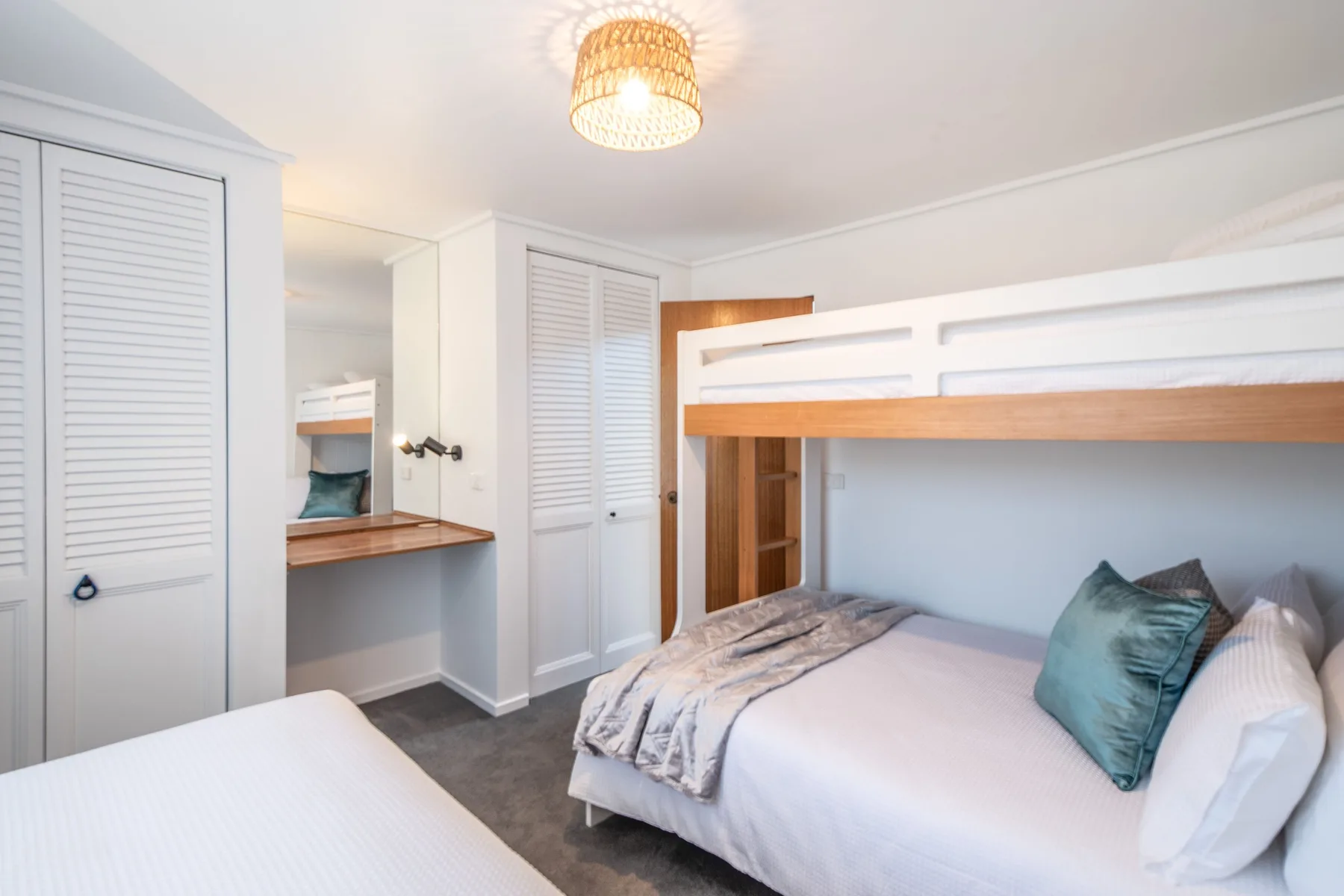 Un dormitorio luminoso con una cama blanca y una litera de madera encima.