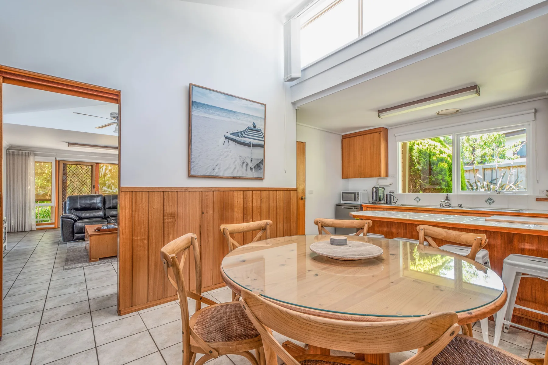 Un comedor luminoso tiene una mesa redonda junto a una encimera de cocina y ventanas.