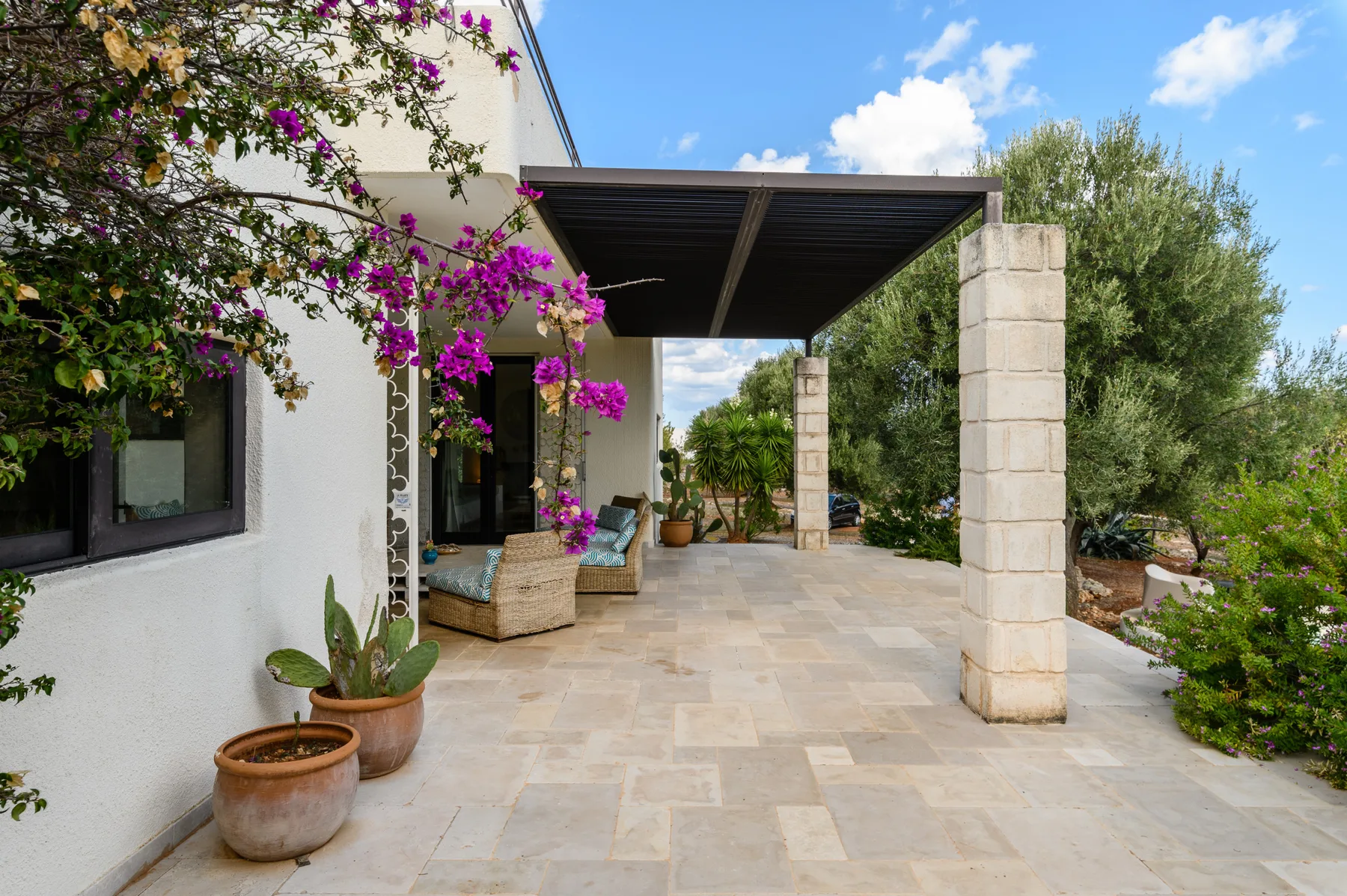 A stone-paved outdoor patio beside the house, shaded by a dark pergola.