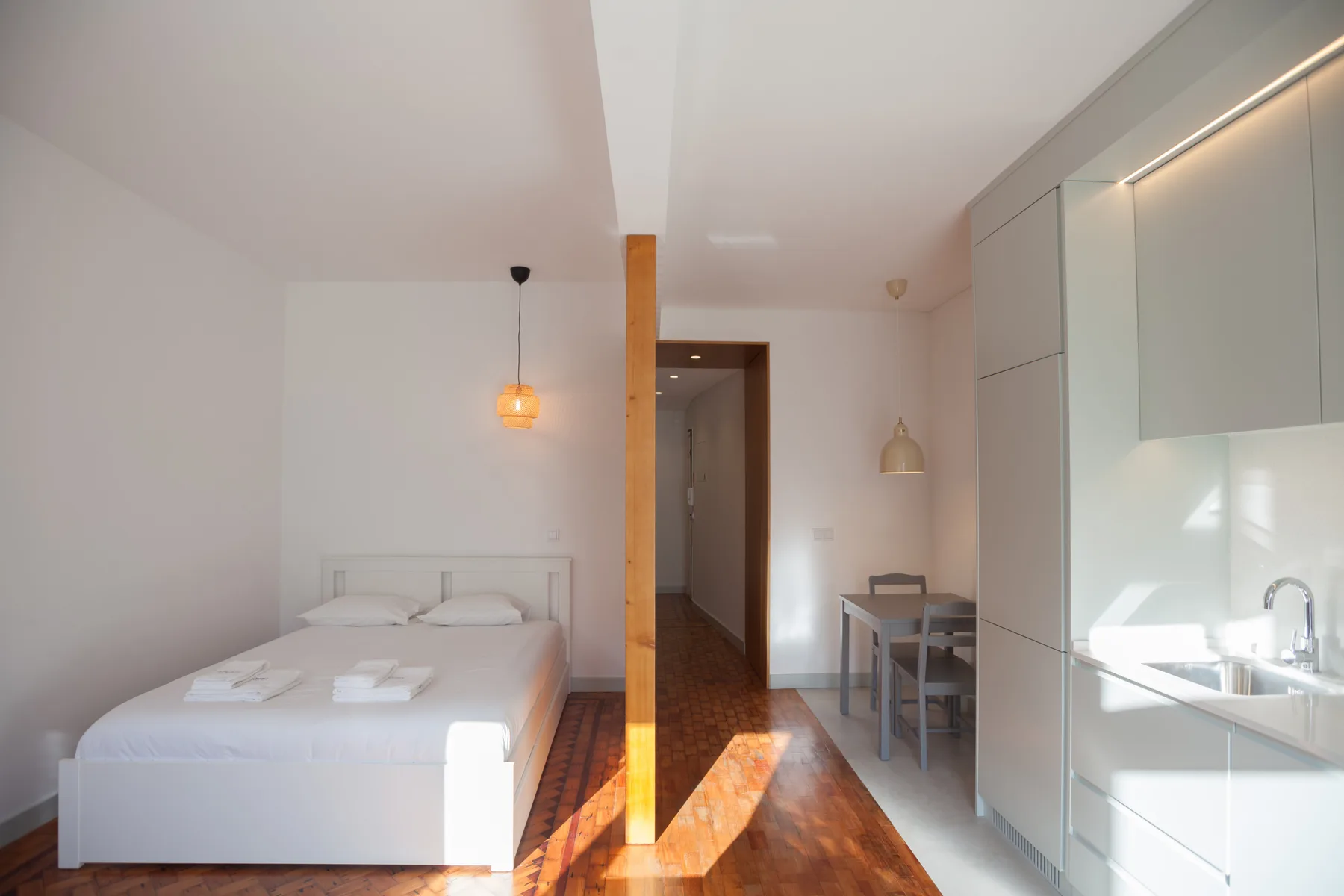 A bright studio room with a bed, a dining area, and built-in cabinets.