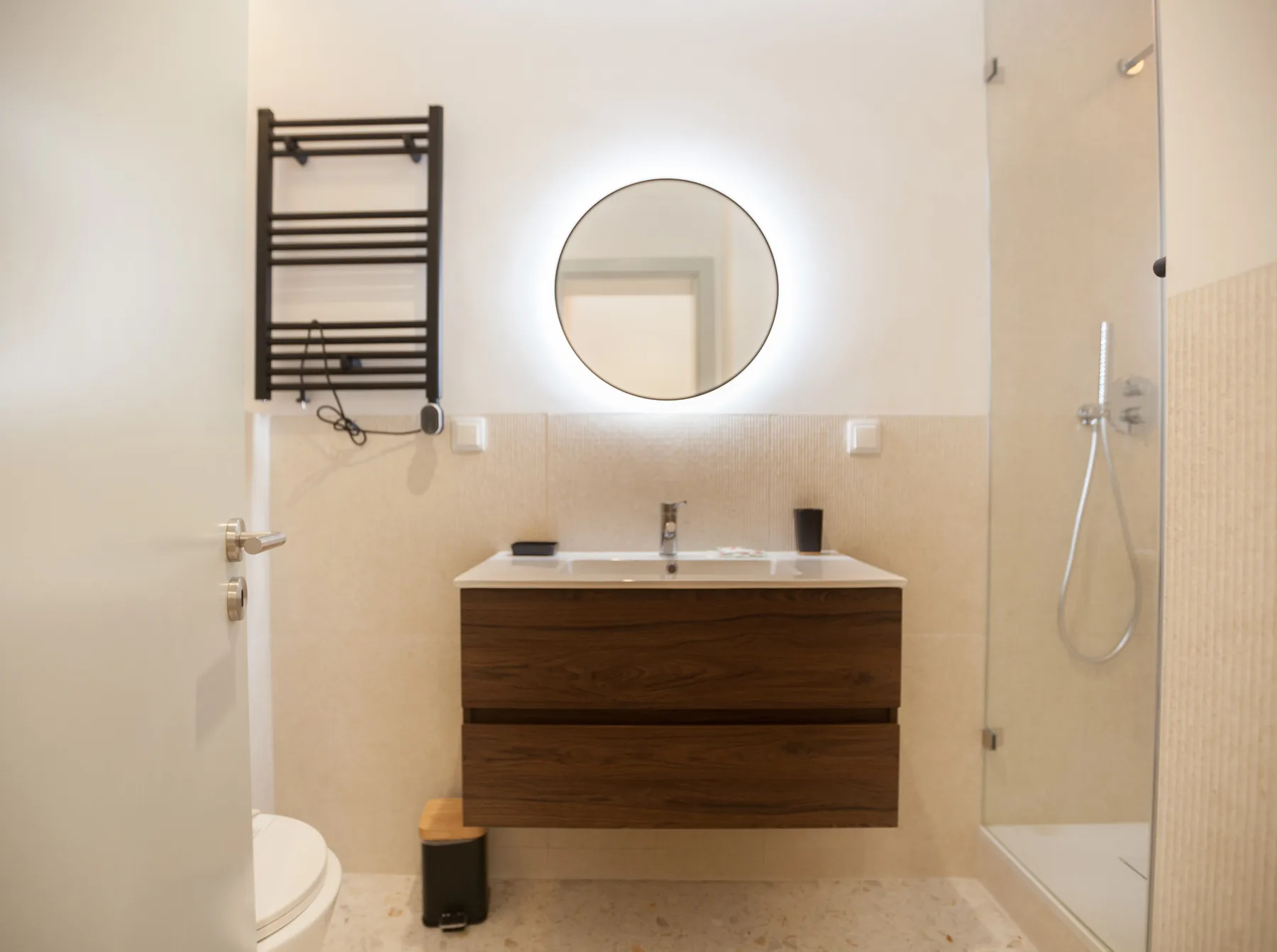 A bathroom with a floating vanity, round mirror, and shower.