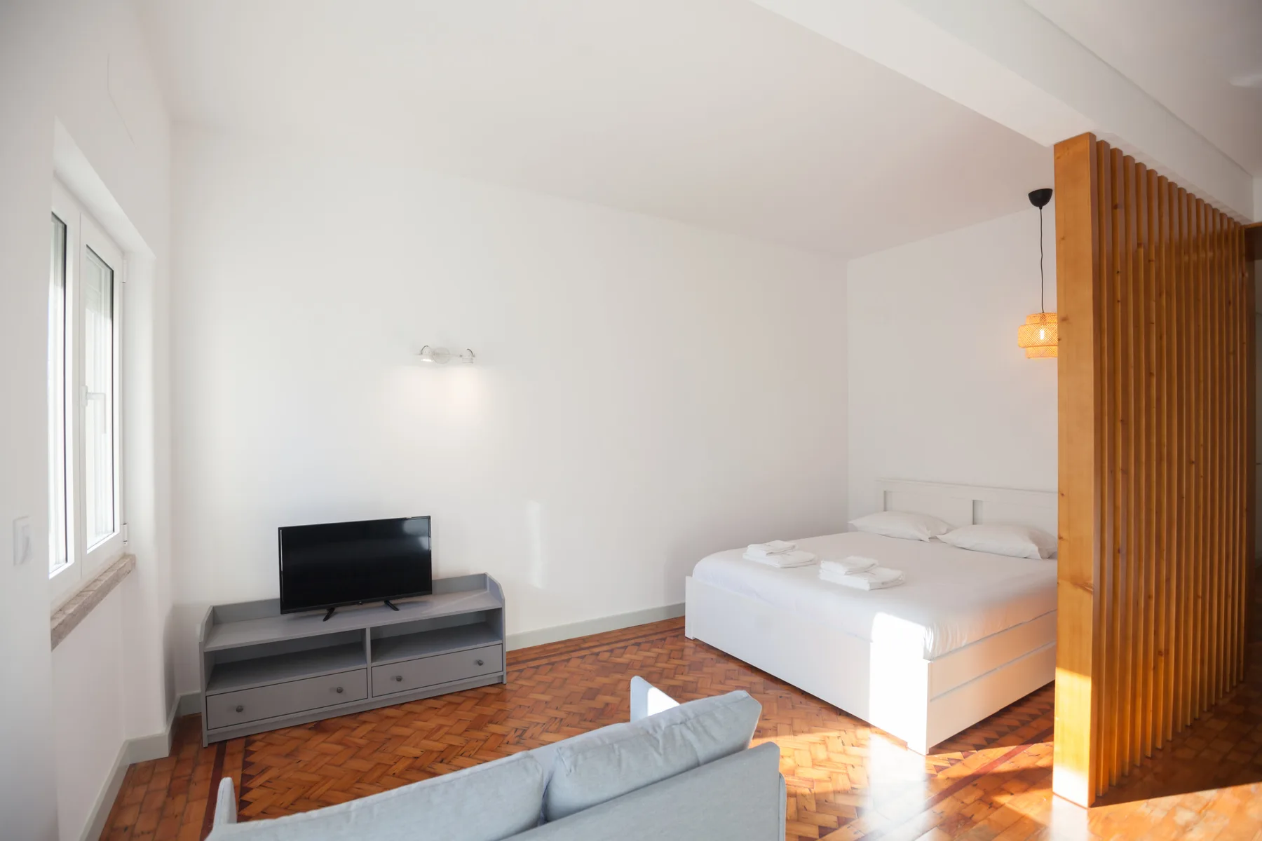 A bright bedroom with a bed, television, and wooden floor.