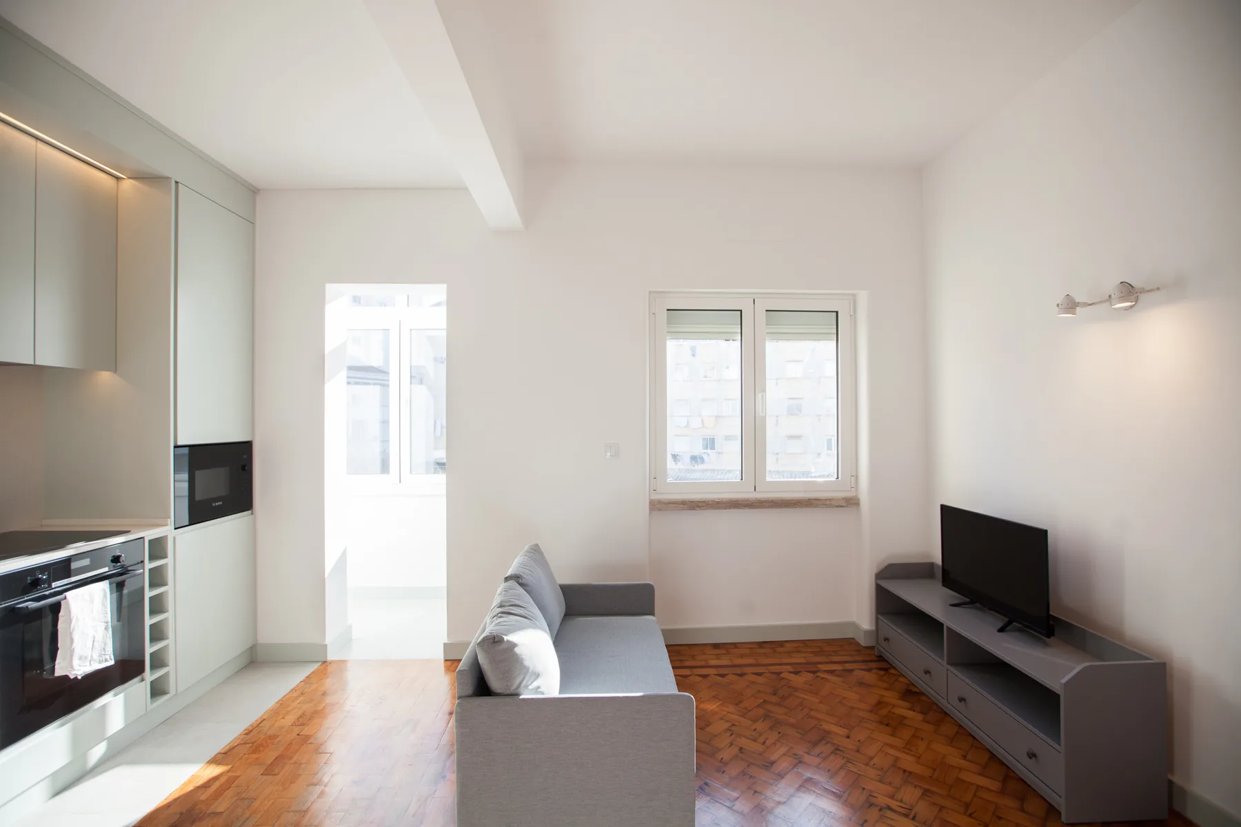 A studio living area with a gray sofa, television, and built-in kitchen.