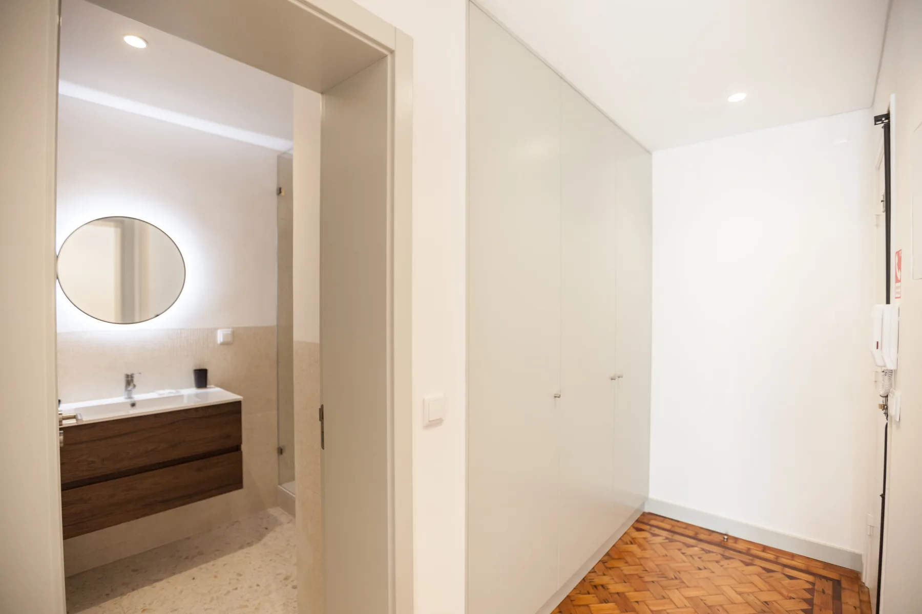 A bright interior hallway opens onto a bathroom with a sink and round mirror.