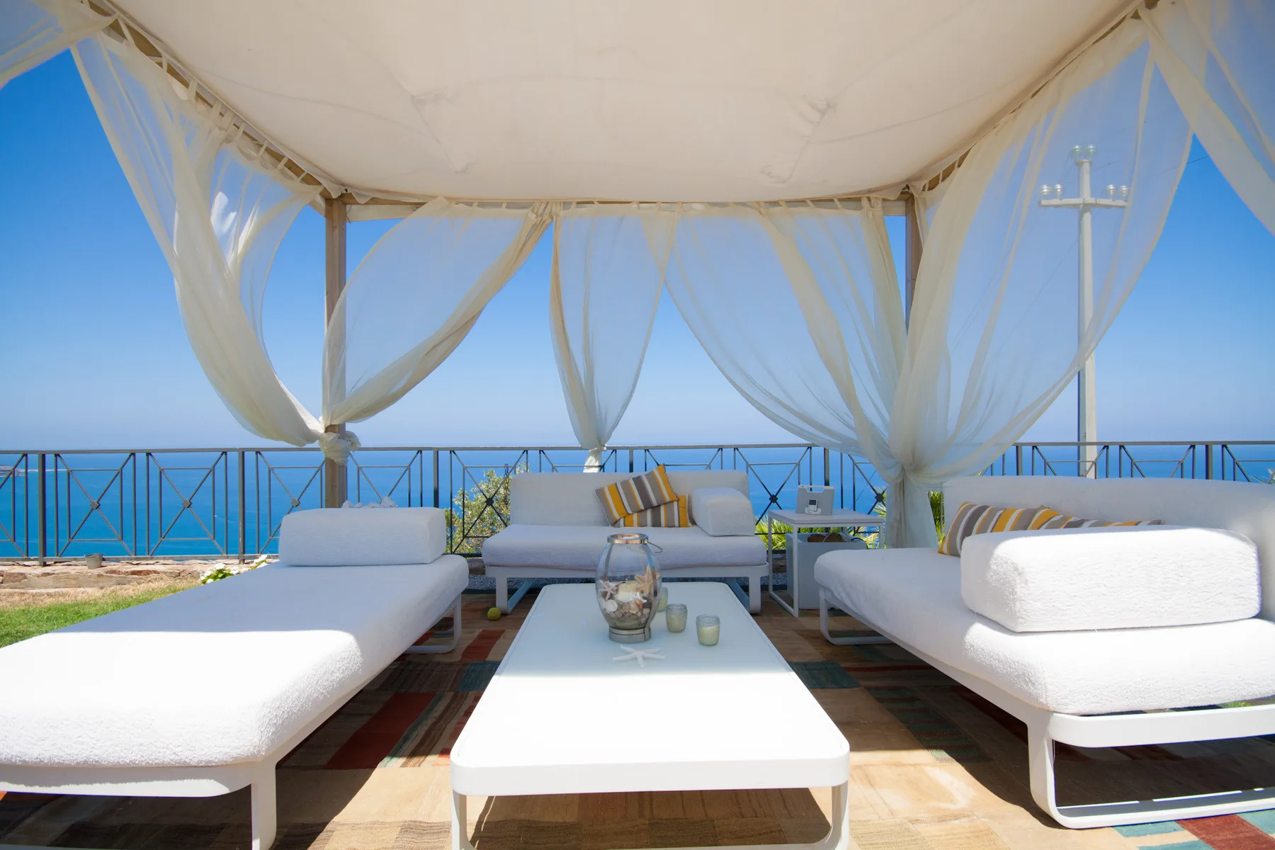 A covered outdoor lounge with white seating and a view of the sea.