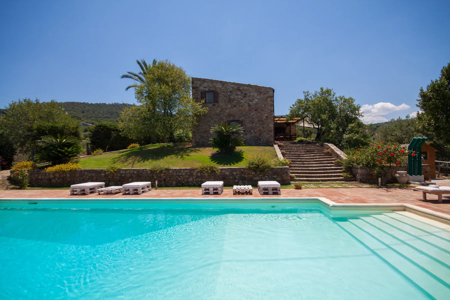 Una piscina al aire libre está frente a edificios de piedra y jardines.