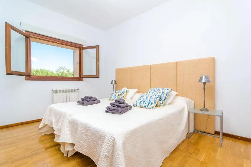 Un dormitorio luminoso con una cama bien tendida bajo una ventana abierta.
