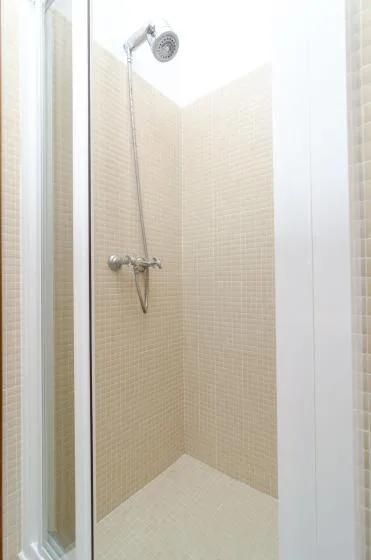 Una ducha con azulejos, ducha de mano y controles montados en la pared.