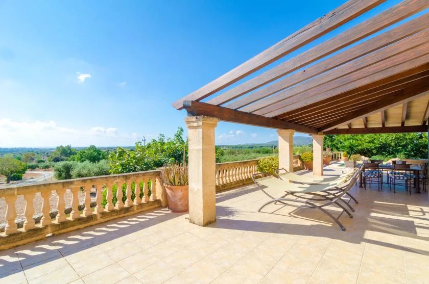 Una terraza soleada con pérgola de madera, asientos reclinables y vistas a la vegetación cercana.