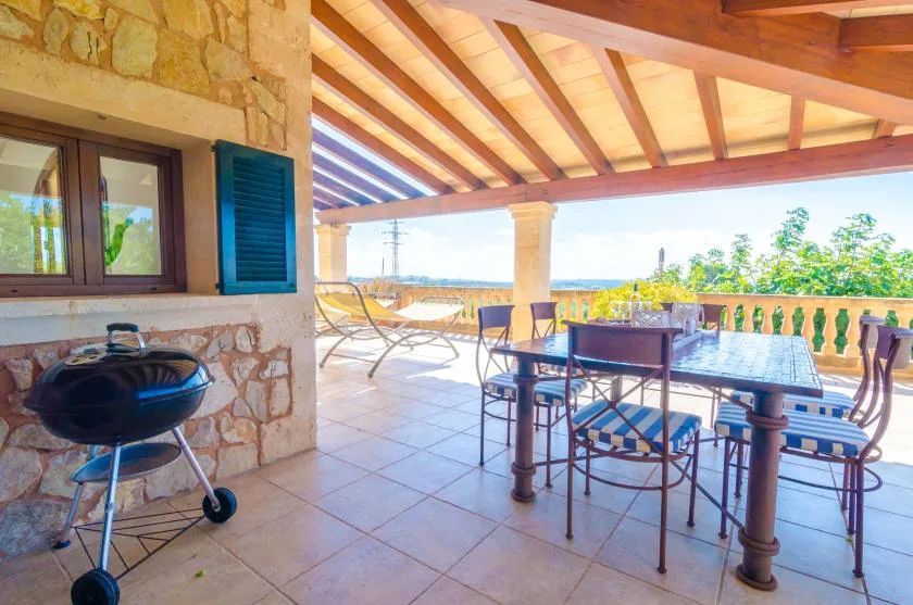 Comedor exterior cubierto con una mesa, sillas y una parrilla.