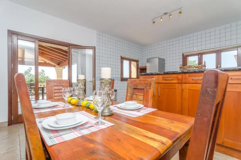Comedor con una mesa de madera preparada con platos junto a una cocina alicatada.