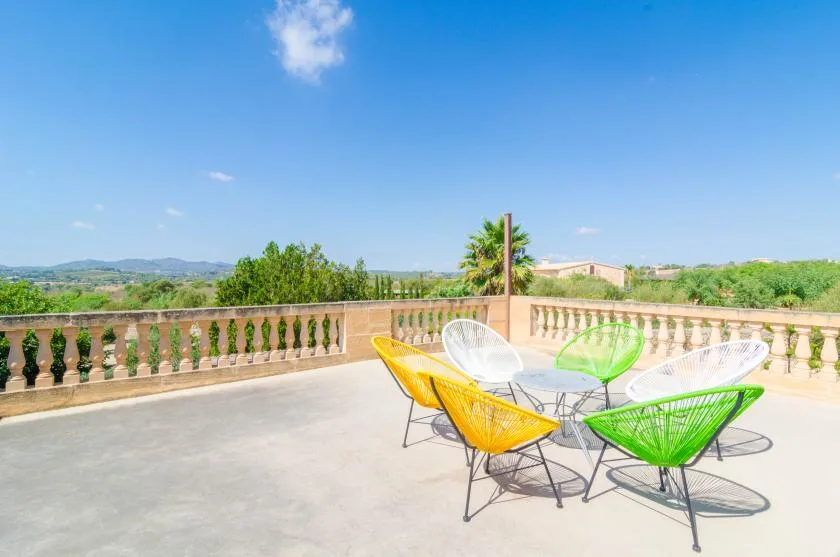 Una terraza abierta tiene asientos de alambre de colores junto a una balaustrada, con vistas al paisaje.