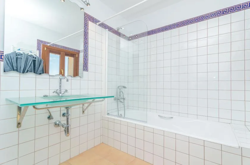 Un baño con azulejos, bañera y estante de vidrio.