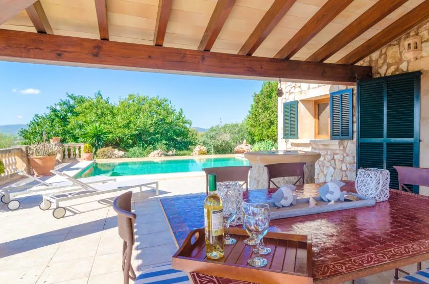 Una zona de comedor exterior cubierta da a una piscina y un paisaje verde.