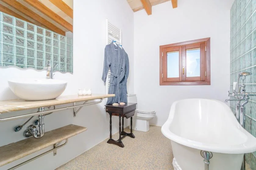 Un baño luminoso con bañera exenta, lavabo y ventana de madera.