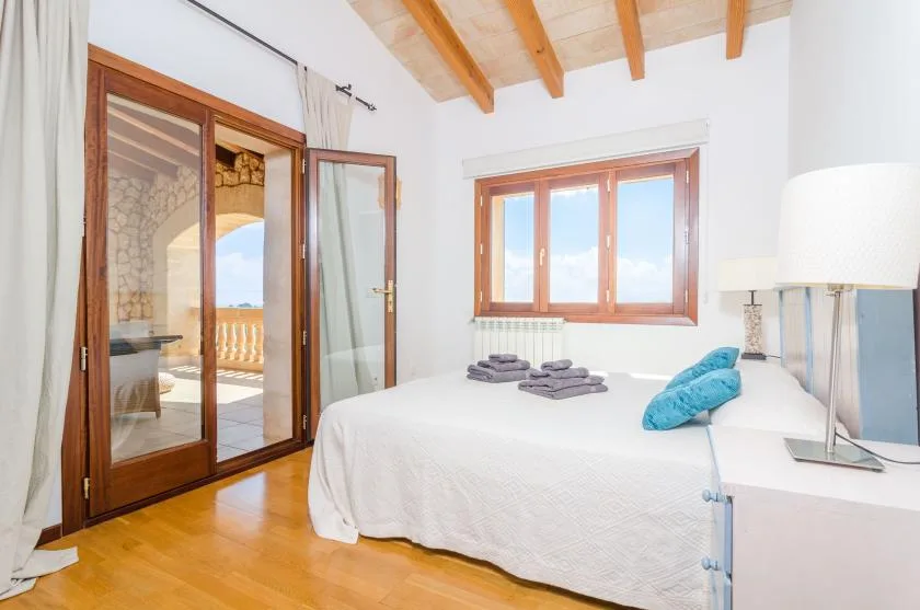 Un dormitorio luminoso con una cama bajo una ventana y vigas de madera en el techo.