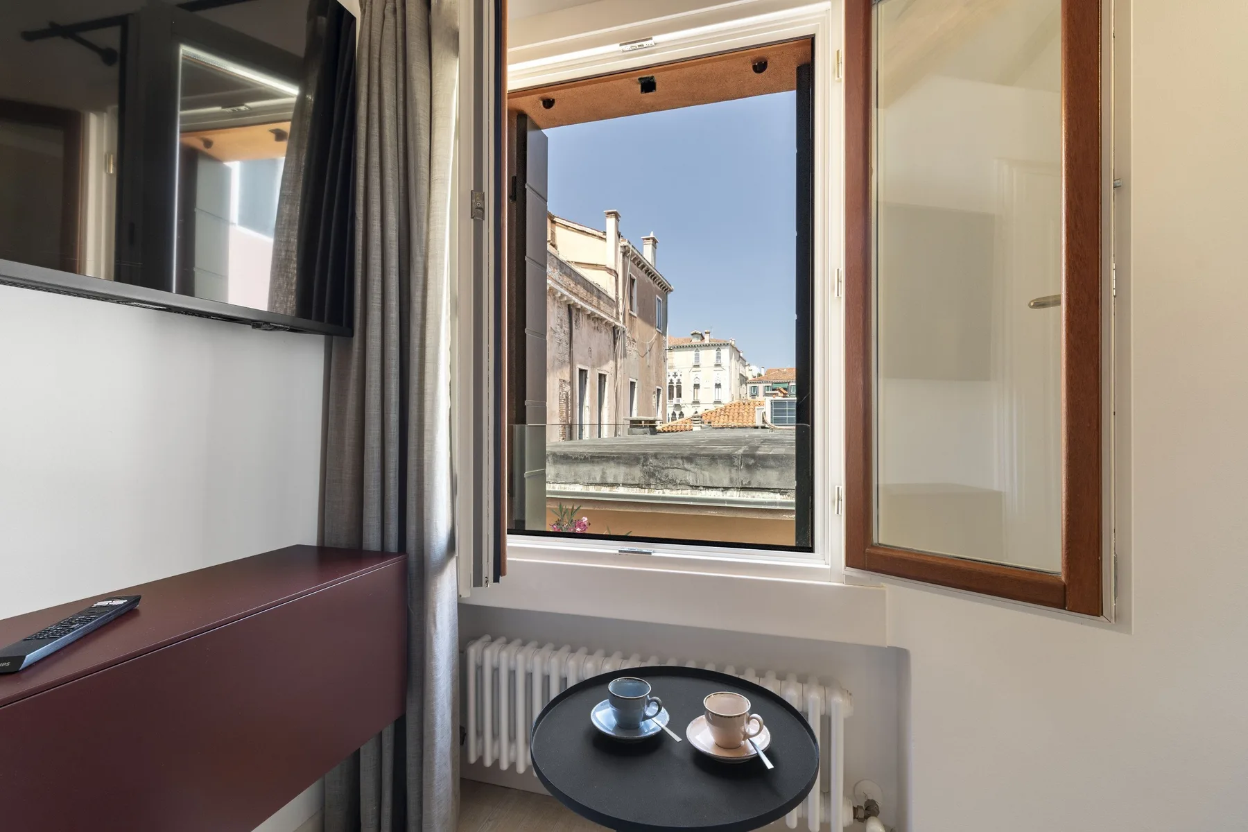 An open window overlooks nearby buildings, with a small table and seating inside.