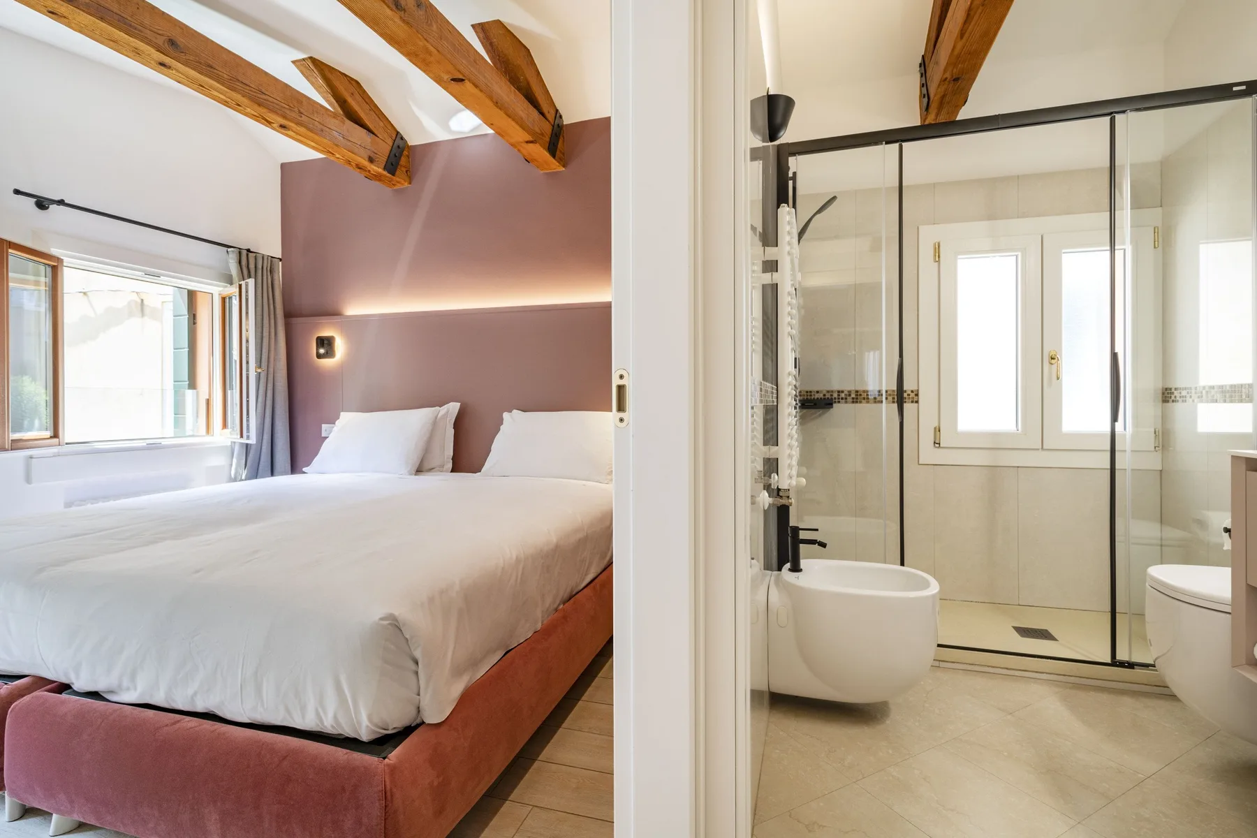 A bedroom with a bed beside a glass-enclosed bathroom.