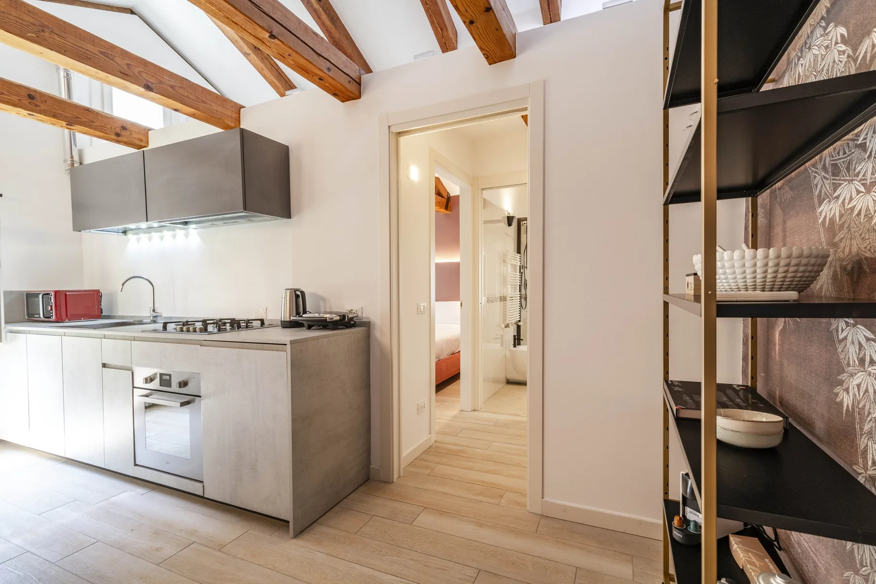 A bright kitchen with white cabinets, a cooktop, and exposed ceiling beams.