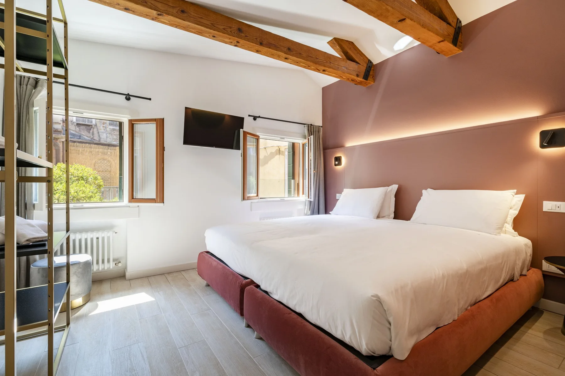 A bedroom with two beds, windows, and exposed wooden ceiling beams.