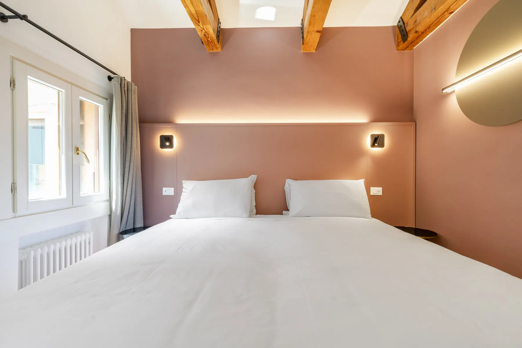 A bedroom with a large bed beneath exposed wooden ceiling beams.