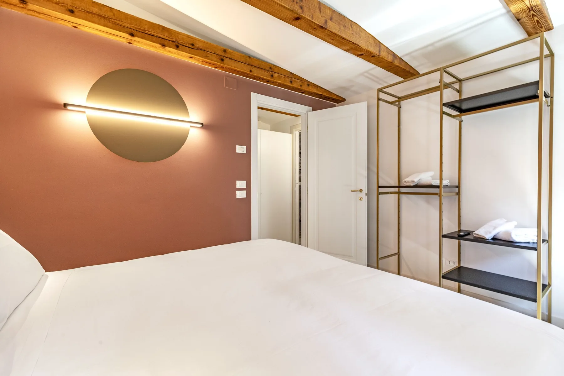 A bedroom with a large bed, a wall light, and open shelving.