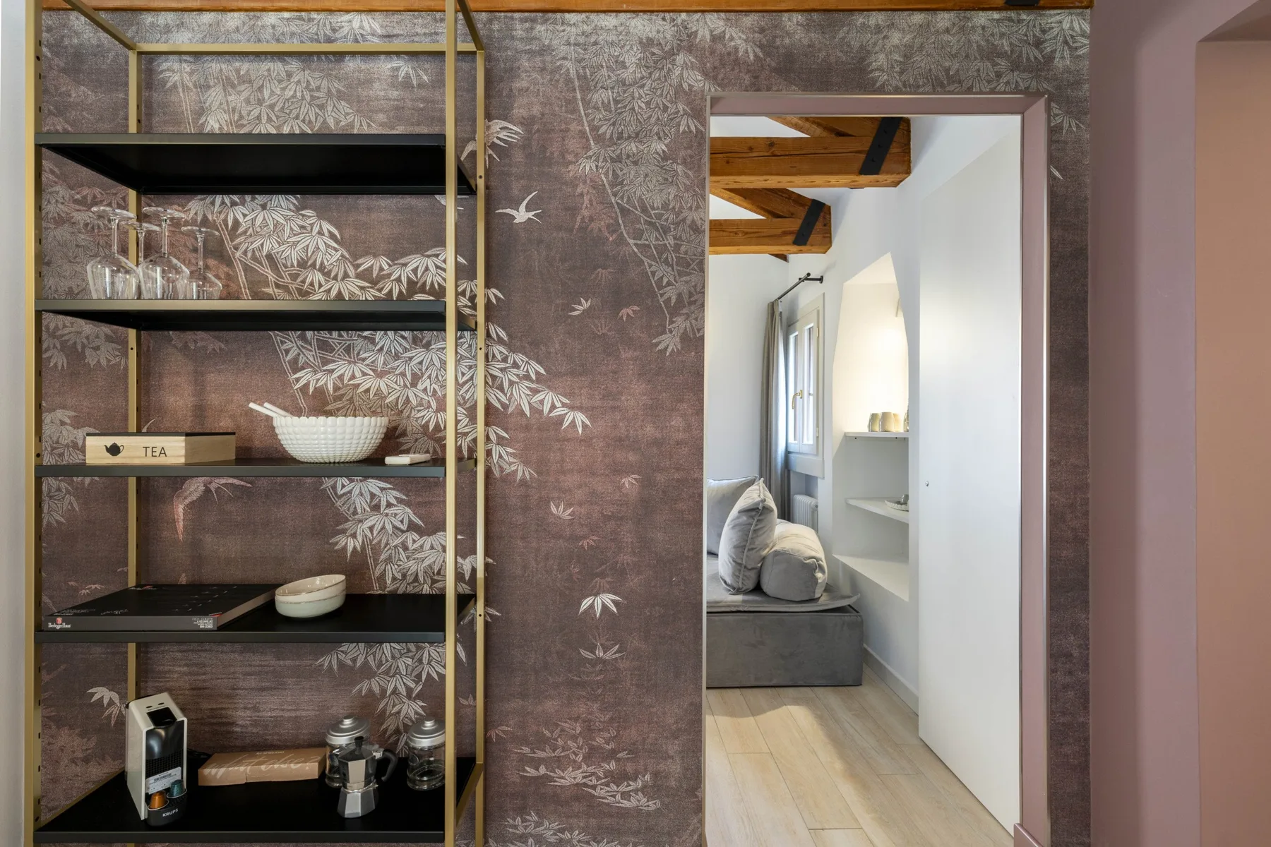 A decorative shelving unit stands beside an open doorway to a bright seating area.