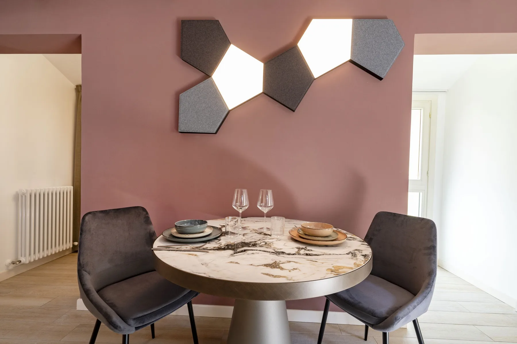 A dining area with a round table and two chairs against a mauve wall.
