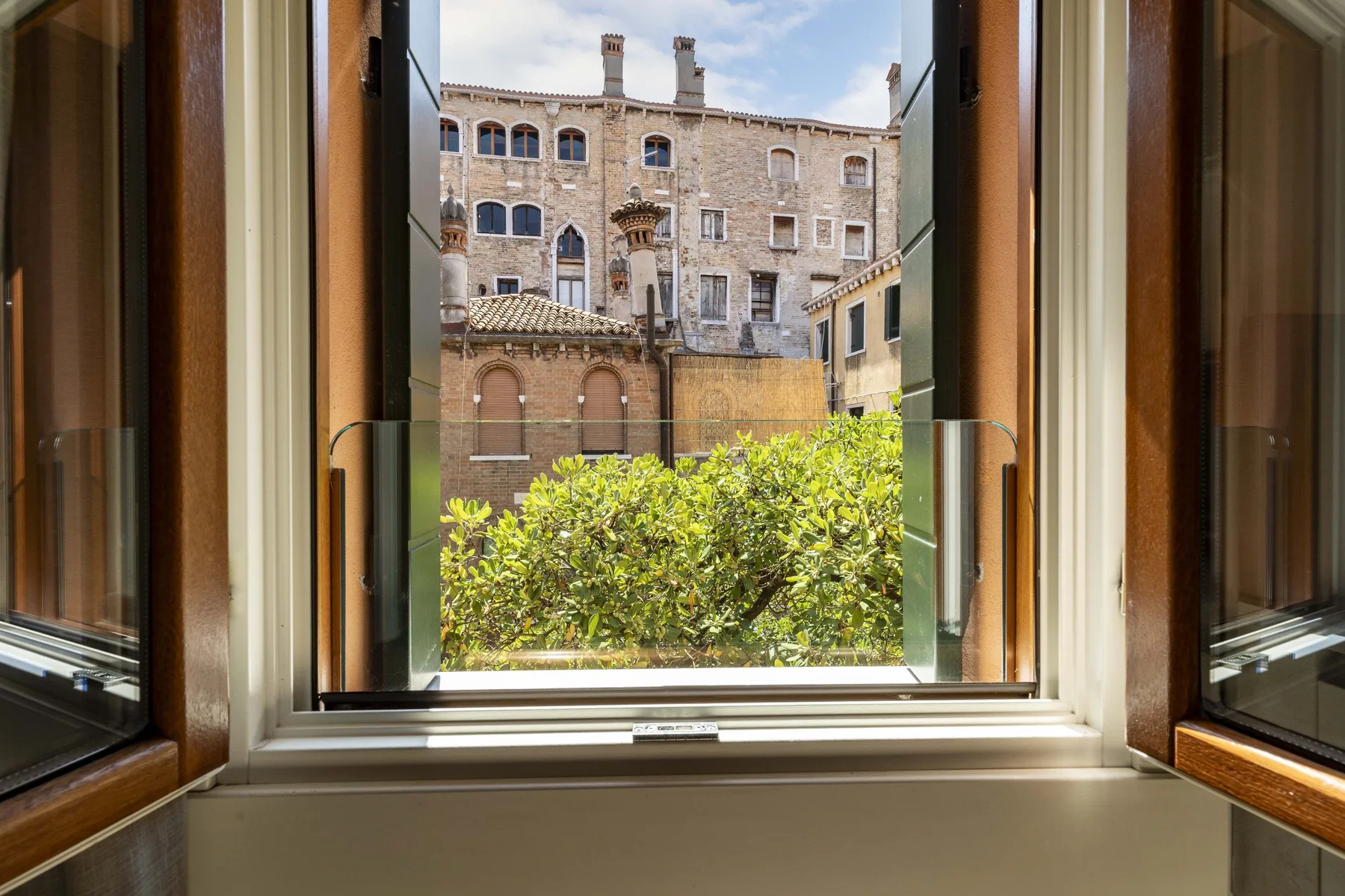 An open window overlooks leafy shrubs and historic-looking buildings.