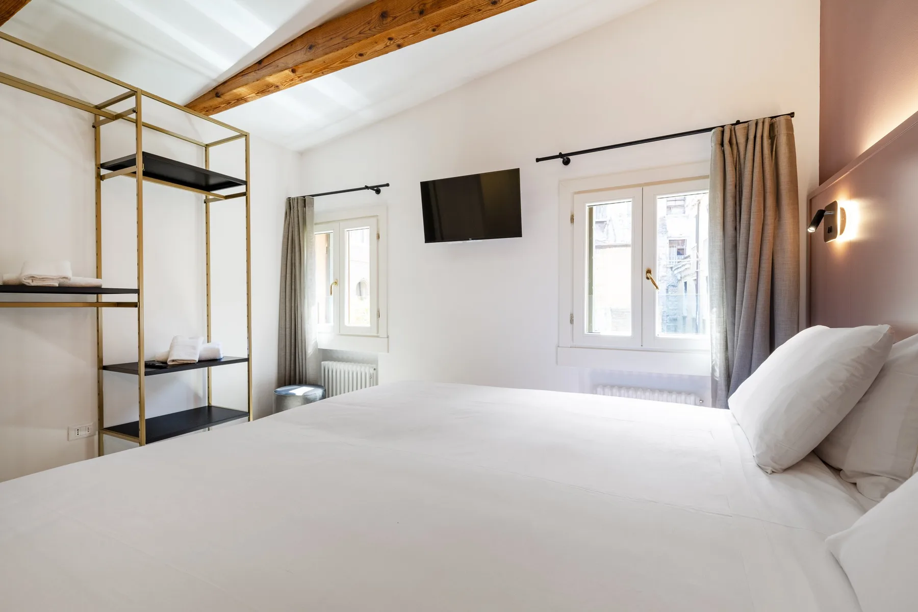 A bright bedroom with a large bed, windows, and open shelving.
