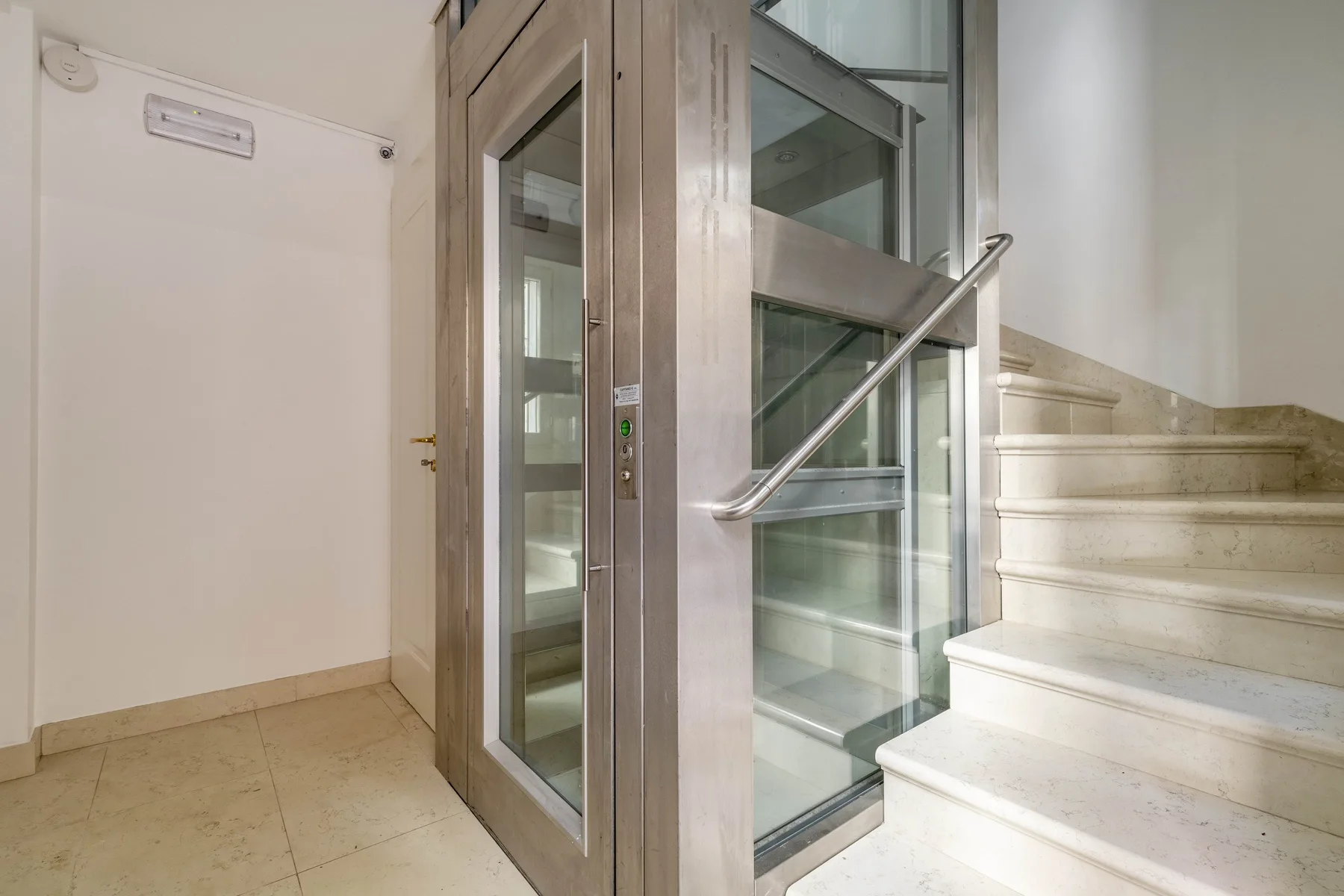 An indoor stairway beside a glass elevator and metal handrail.