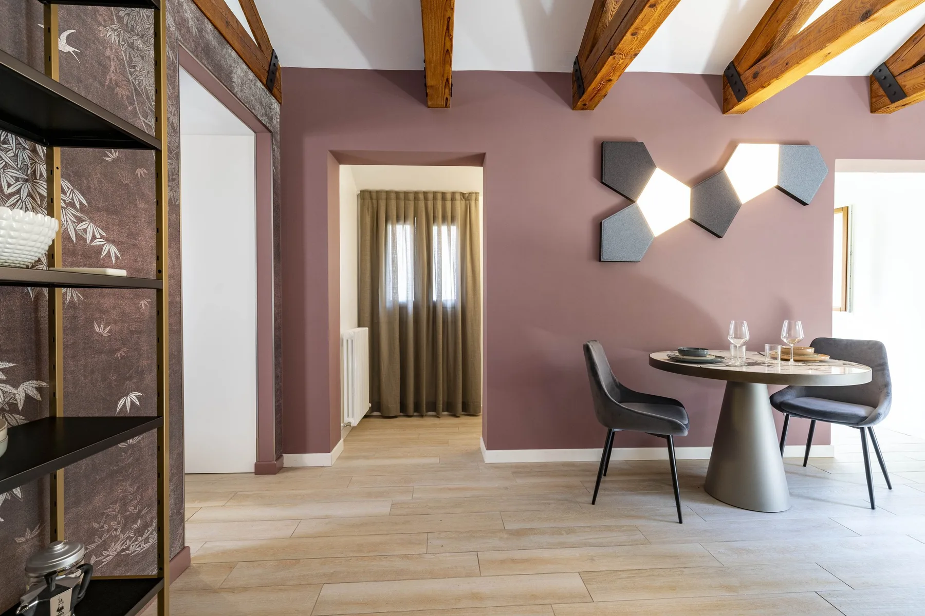 A dining area with a round table, chairs, and exposed wooden ceiling beams.