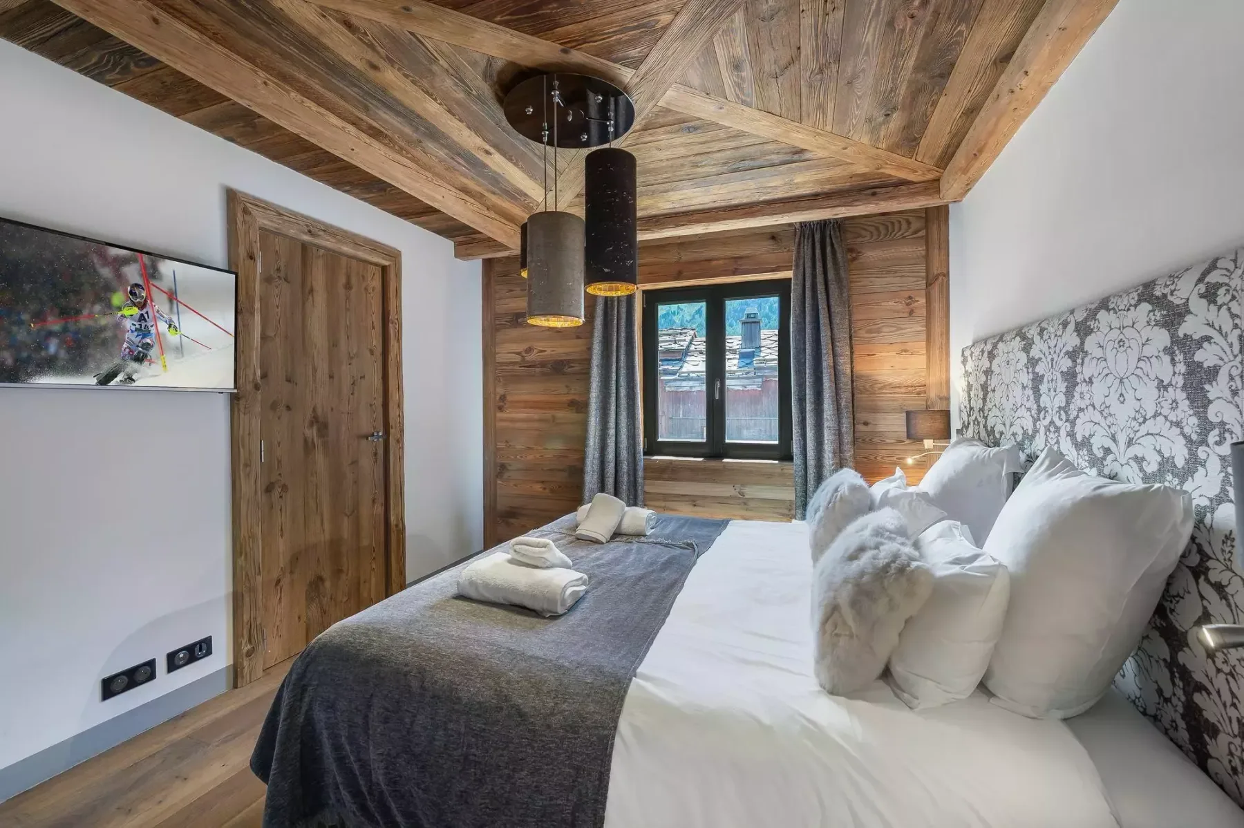 A bedroom with a bed beneath a wooden ceiling and a window.