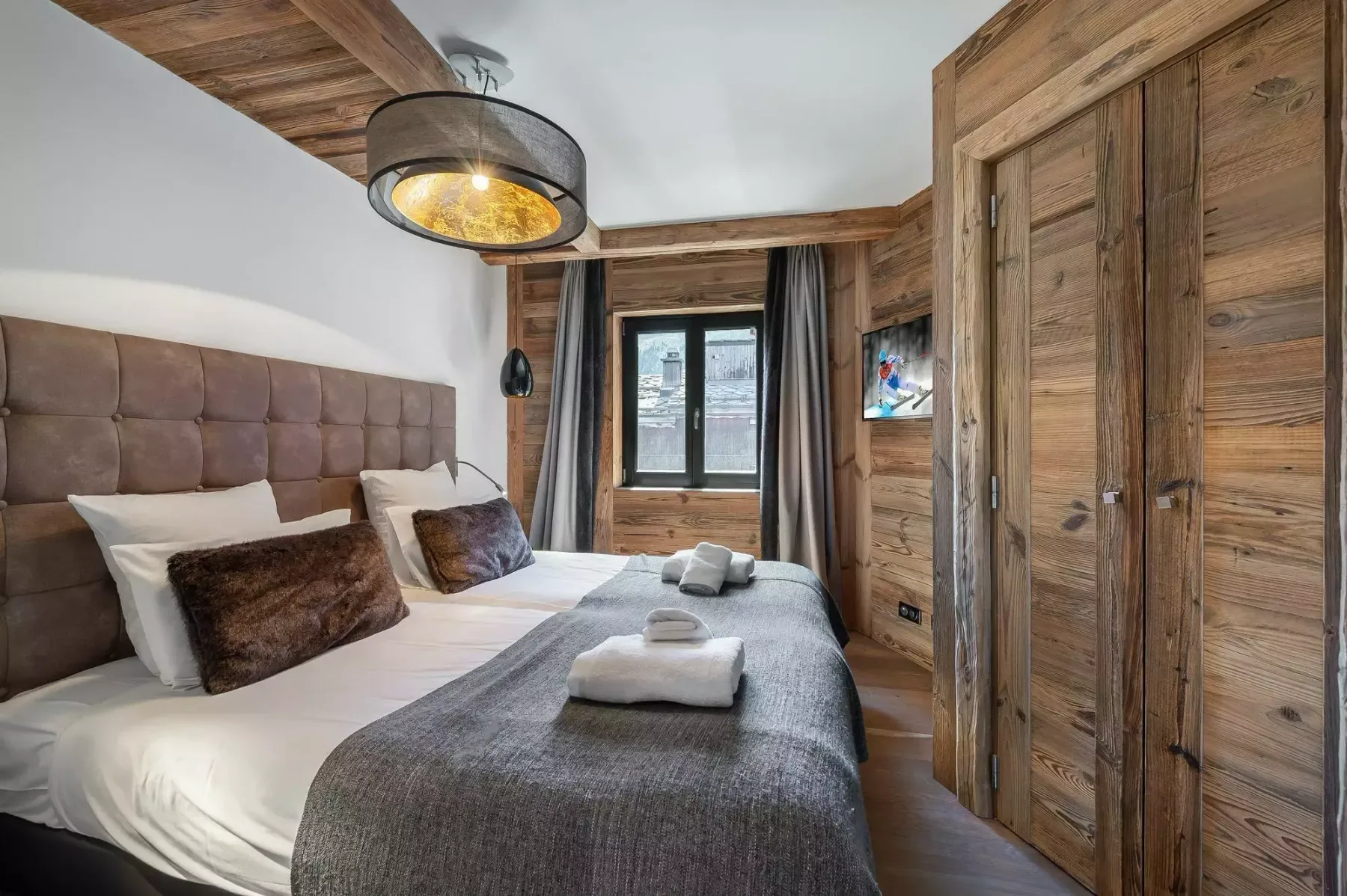 A bedroom with a neatly made bed and a window framed by wood paneling.