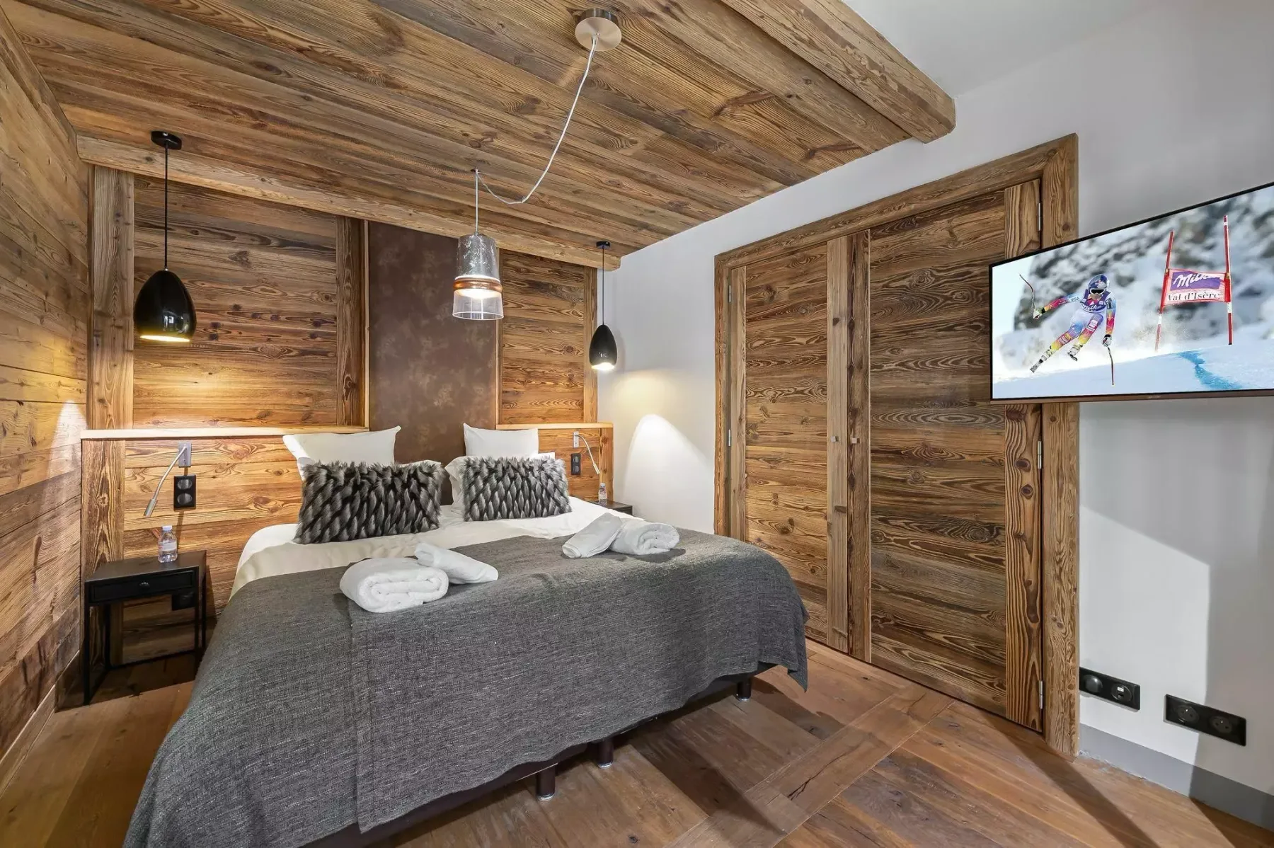 A bedroom with a double bed, wood-paneled walls, and a television.
