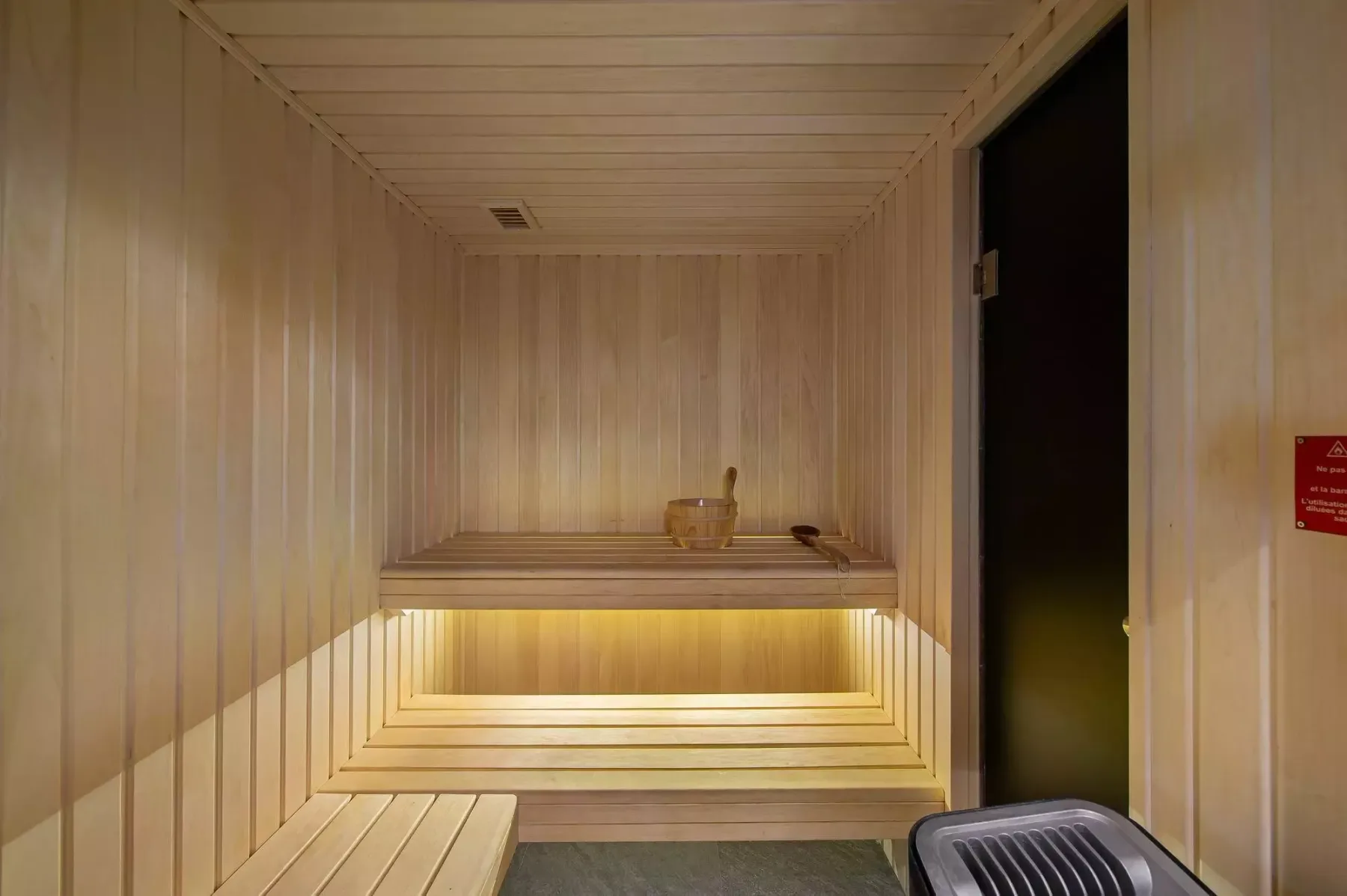 A wood-paneled sauna room with tiered benches and a small heater.