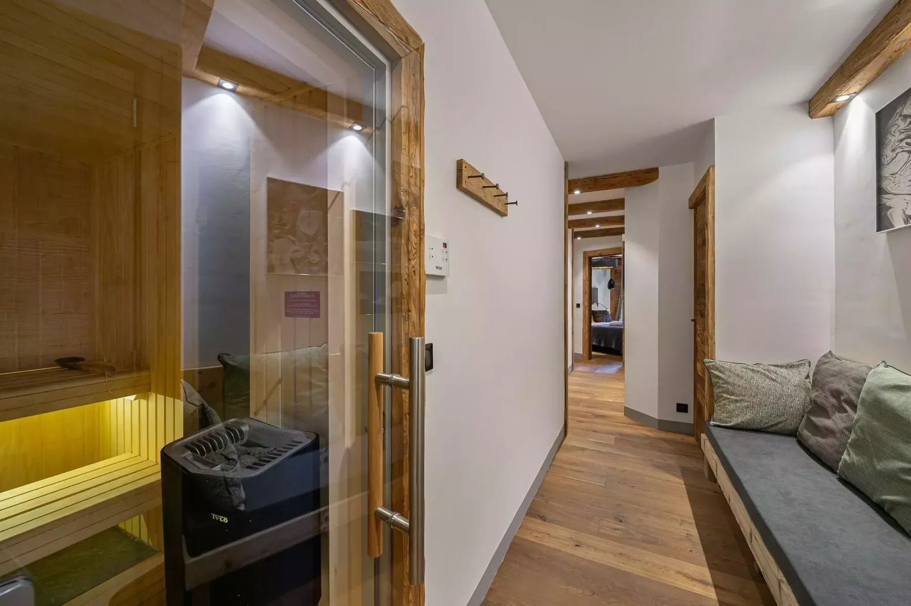 A hallway with a glass-fronted sauna and seating along the wall.