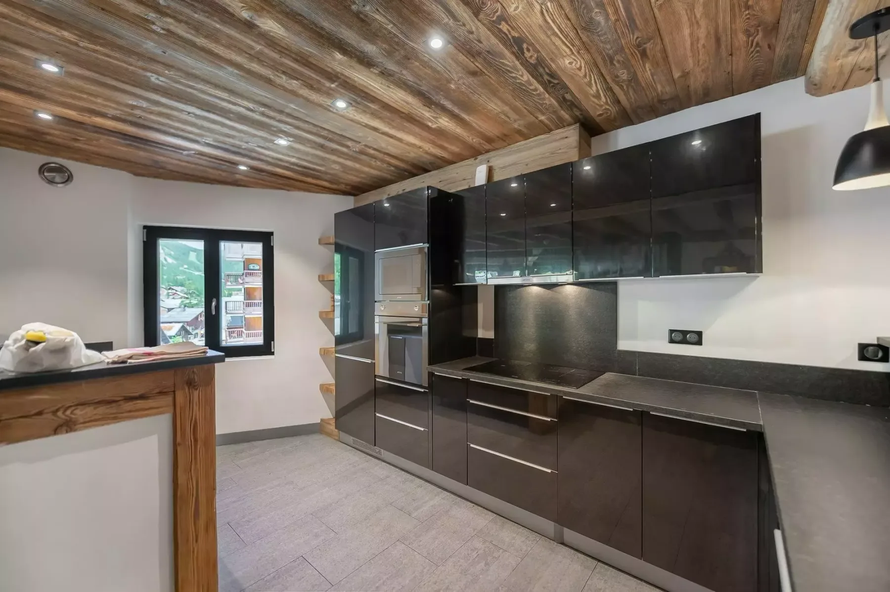 A modern kitchen with dark cabinetry, a countertop, and a wood-paneled ceiling.
