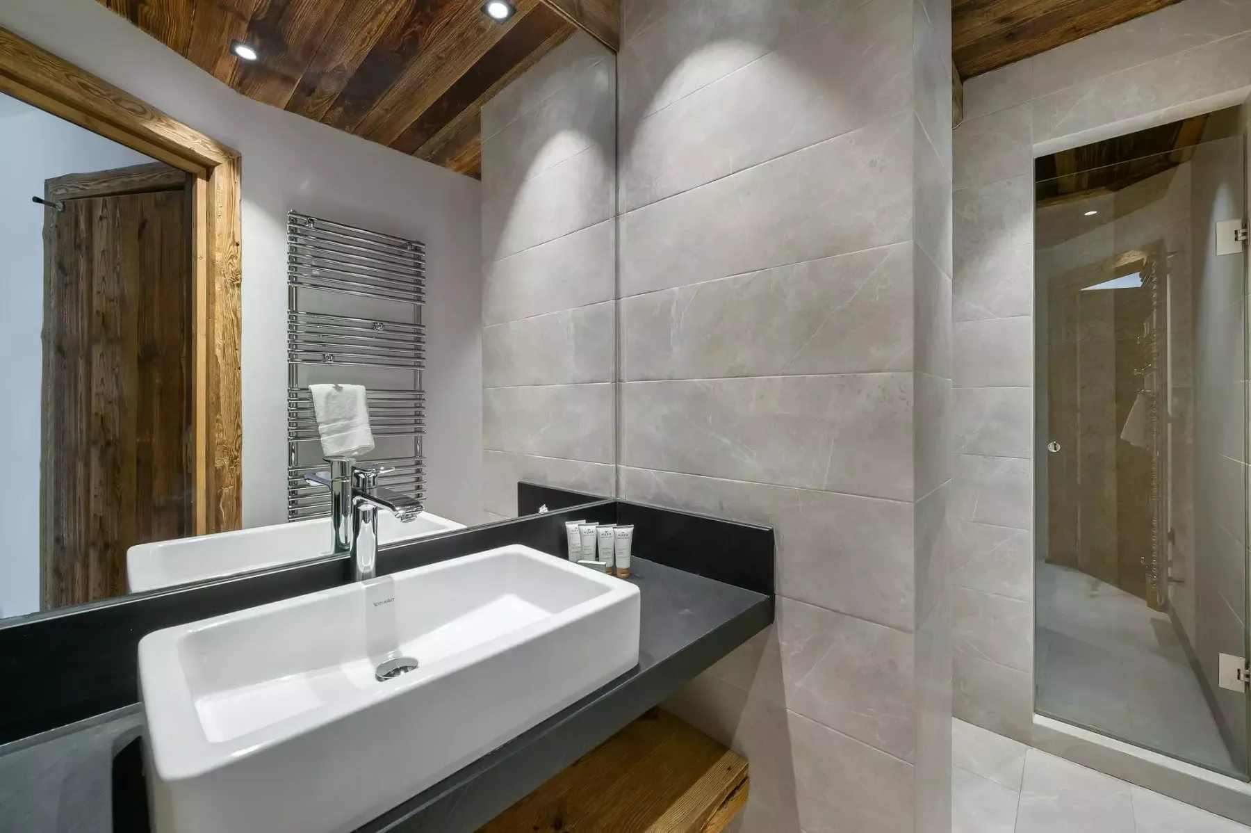 A modern bathroom with a white sink, tiled walls, and a glass shower.