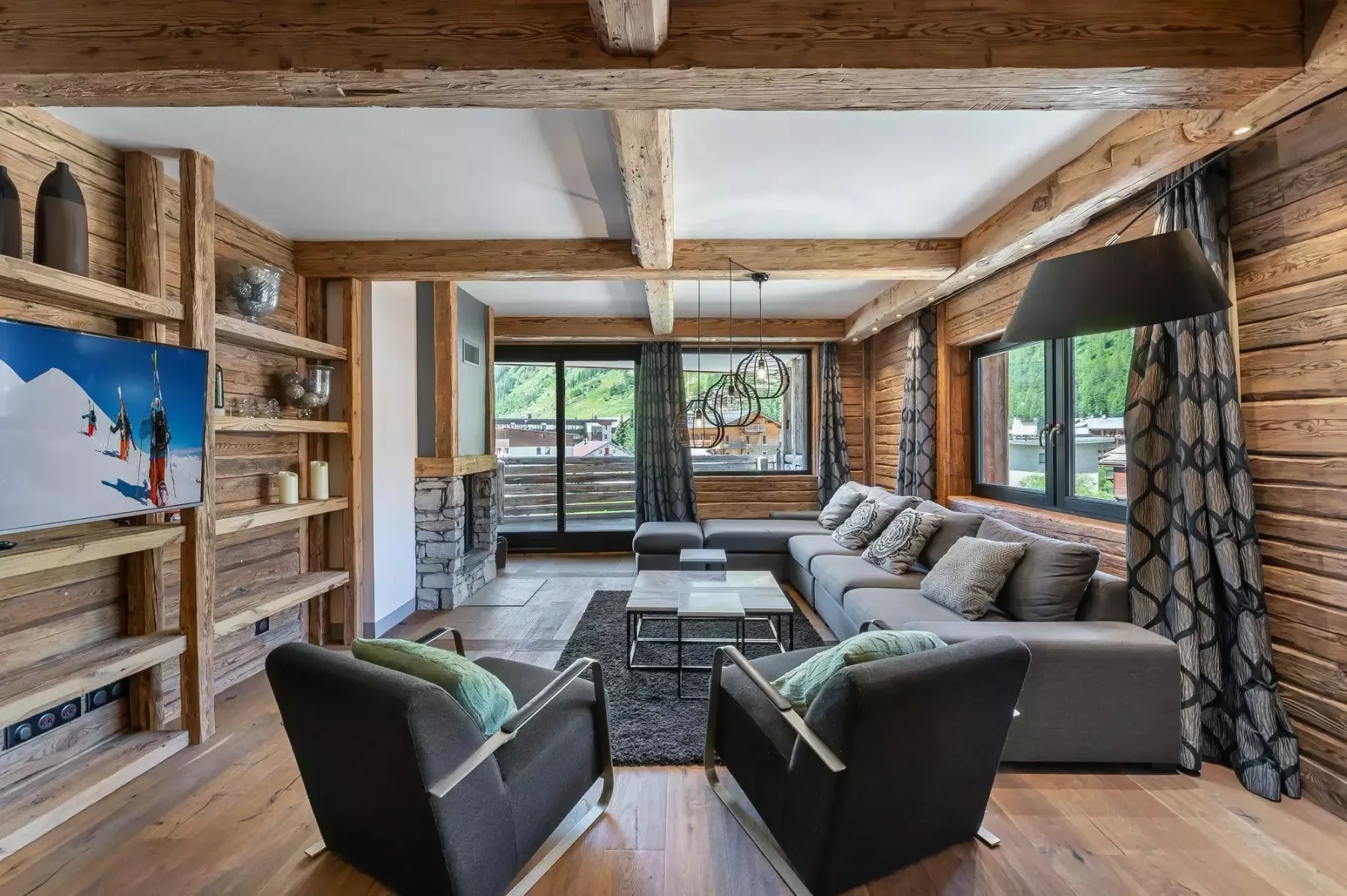 A wood-paneled living room with a seating area, television, and large windows.