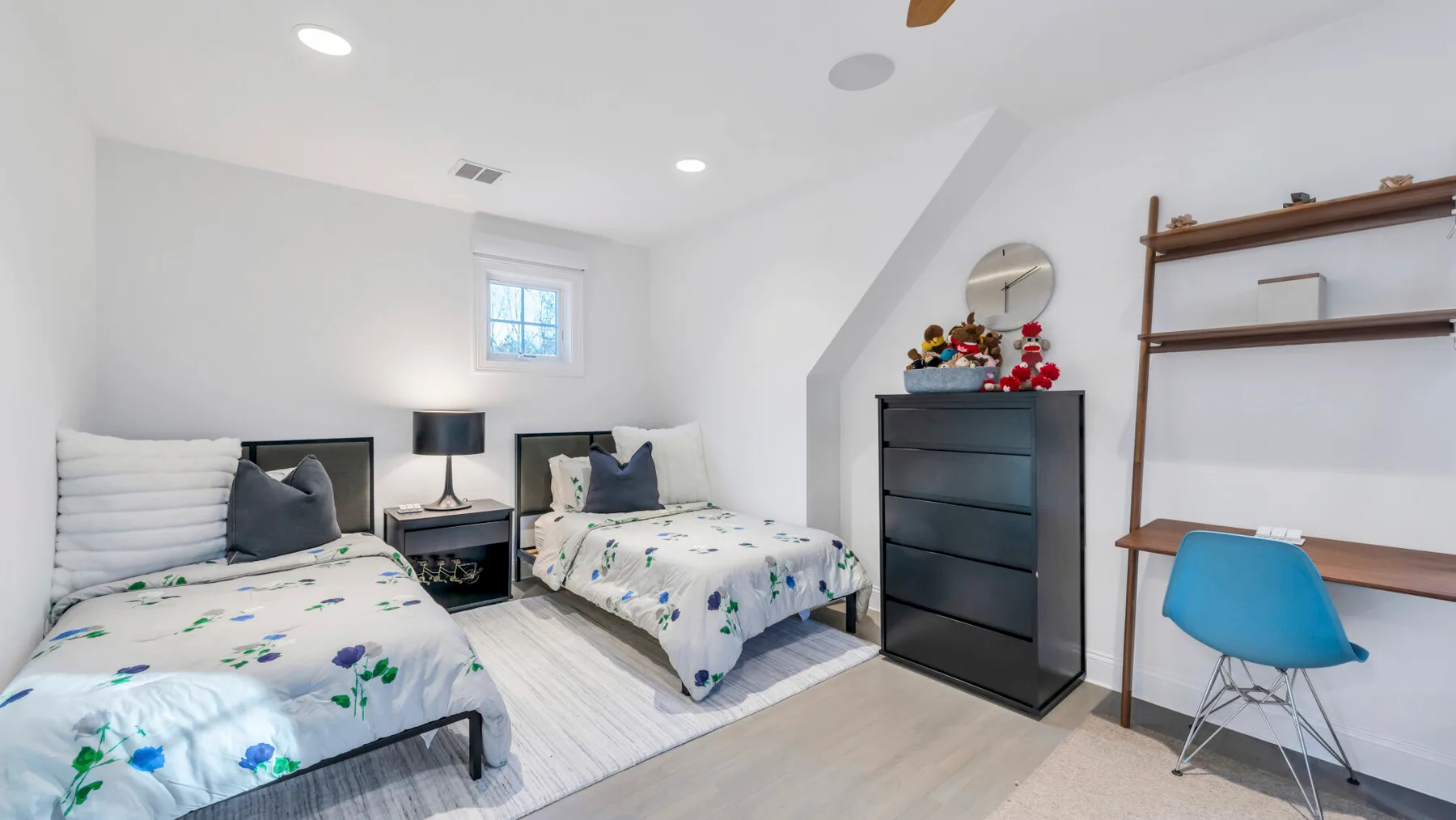 A bright bedroom with two beds, a dresser, and a desk.
