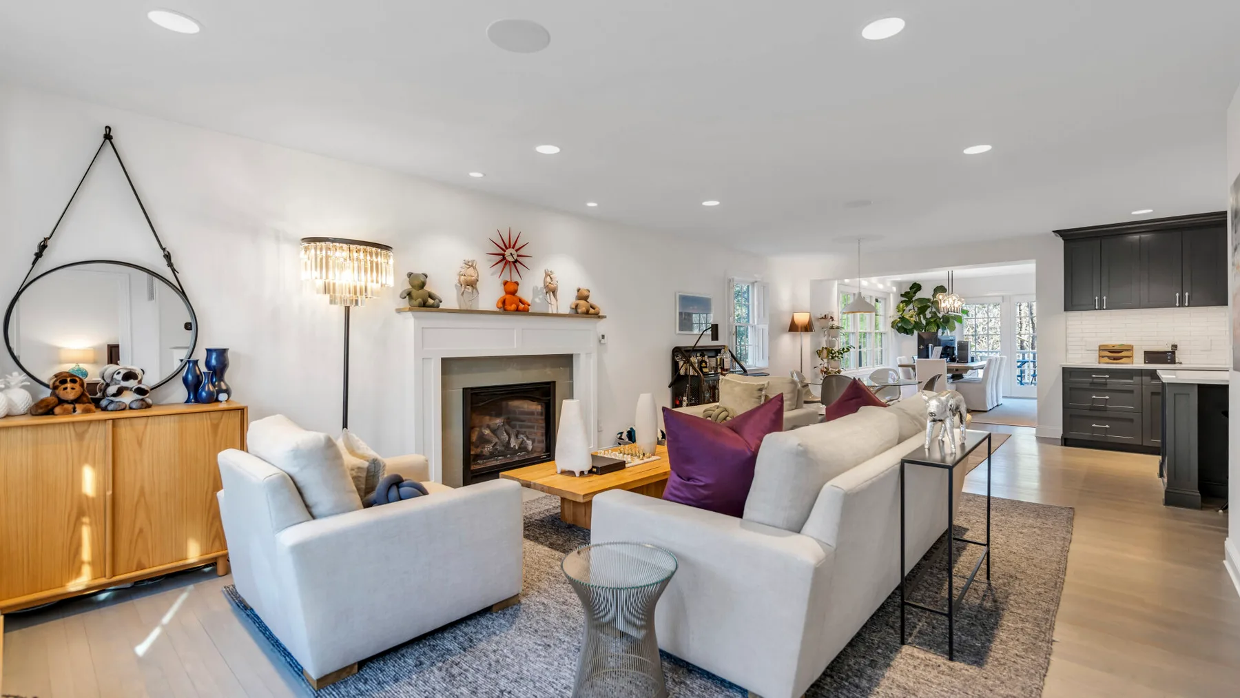 A bright living room with seating around a fireplace and an open kitchen beyond.