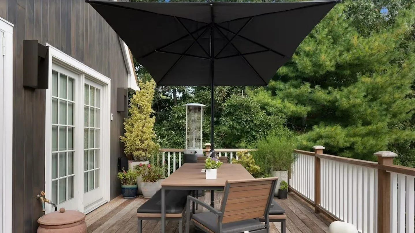 An outdoor deck with a dining table beneath a large umbrella.