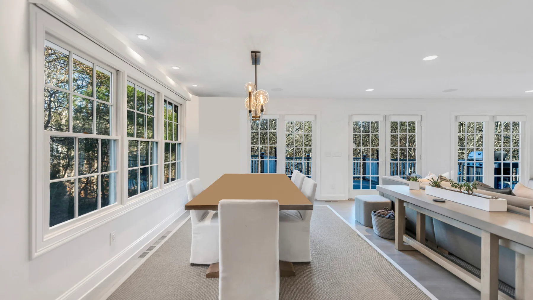 A bright dining area with a long table beside large windows.