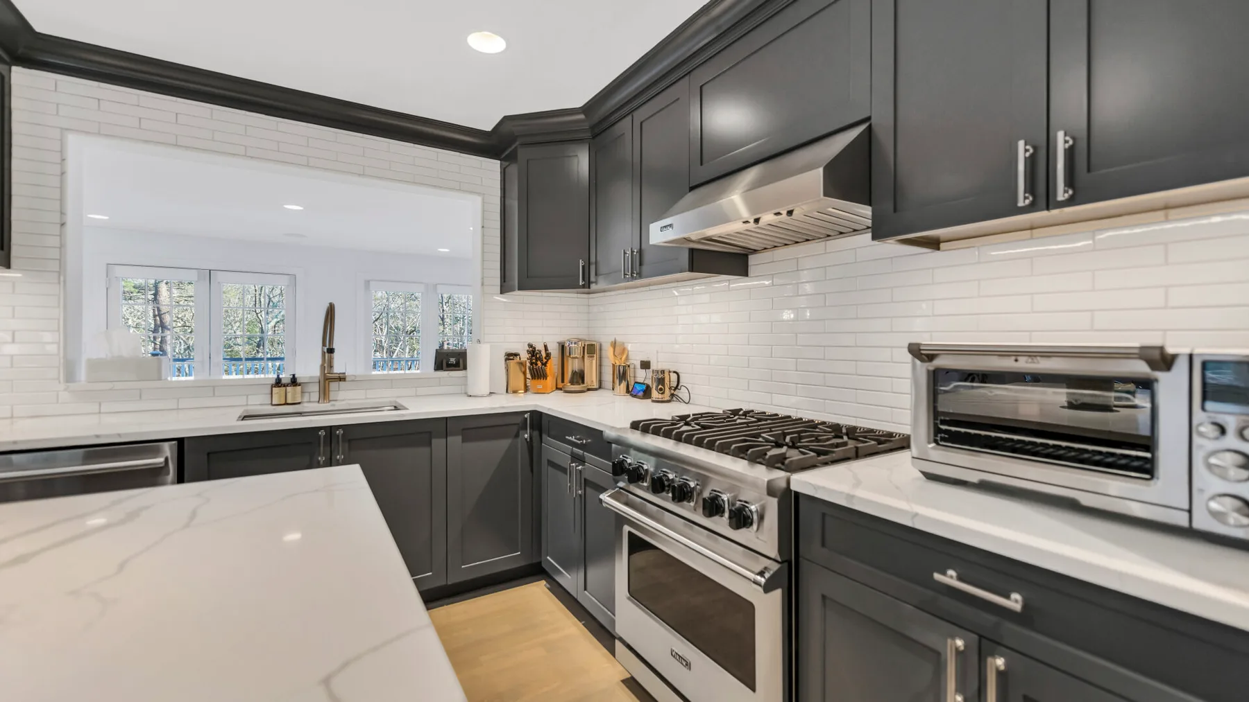 A modern kitchen with dark cabinets, a central range, and windows above the sink.