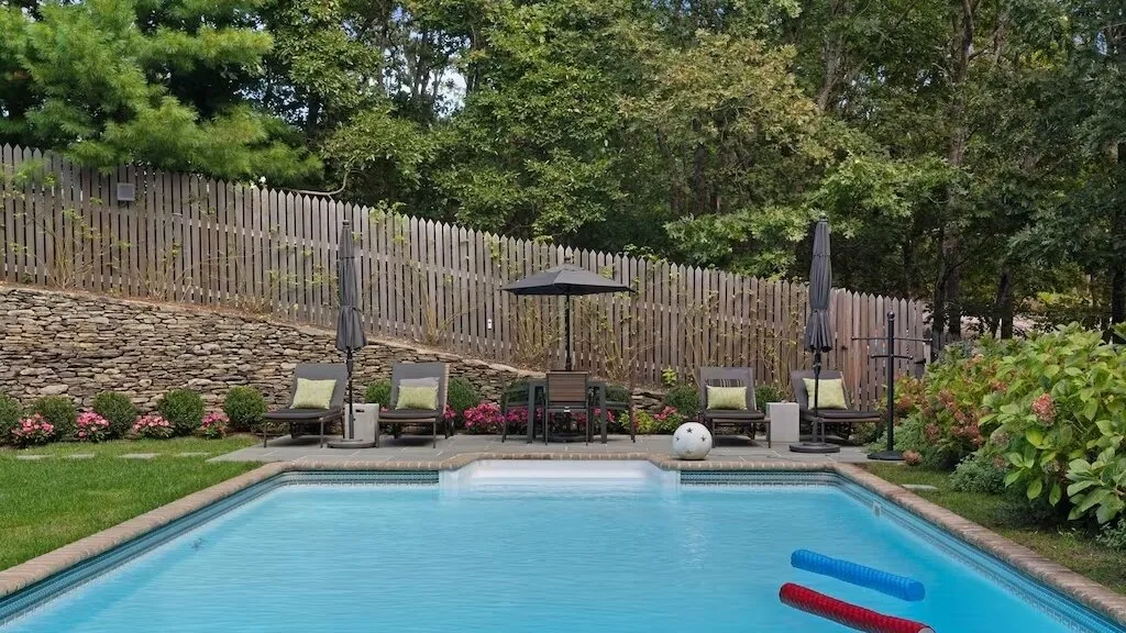 An outdoor swimming pool with lounge seating and greenery around it.