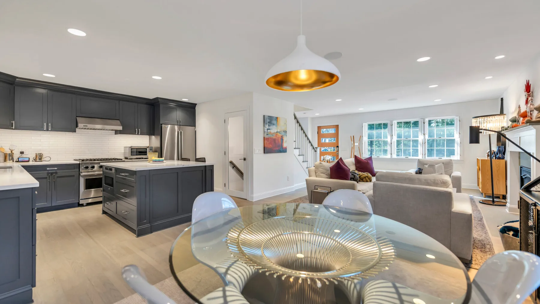 An open-plan kitchen and living area with a glass dining table in the foreground.