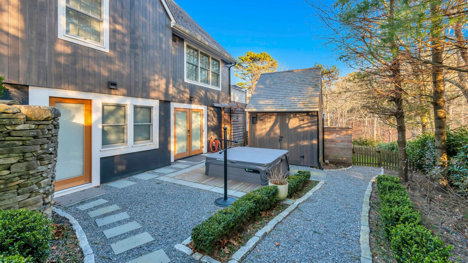 A dark-sided house and small outbuilding sit beside a gravel path and patio.