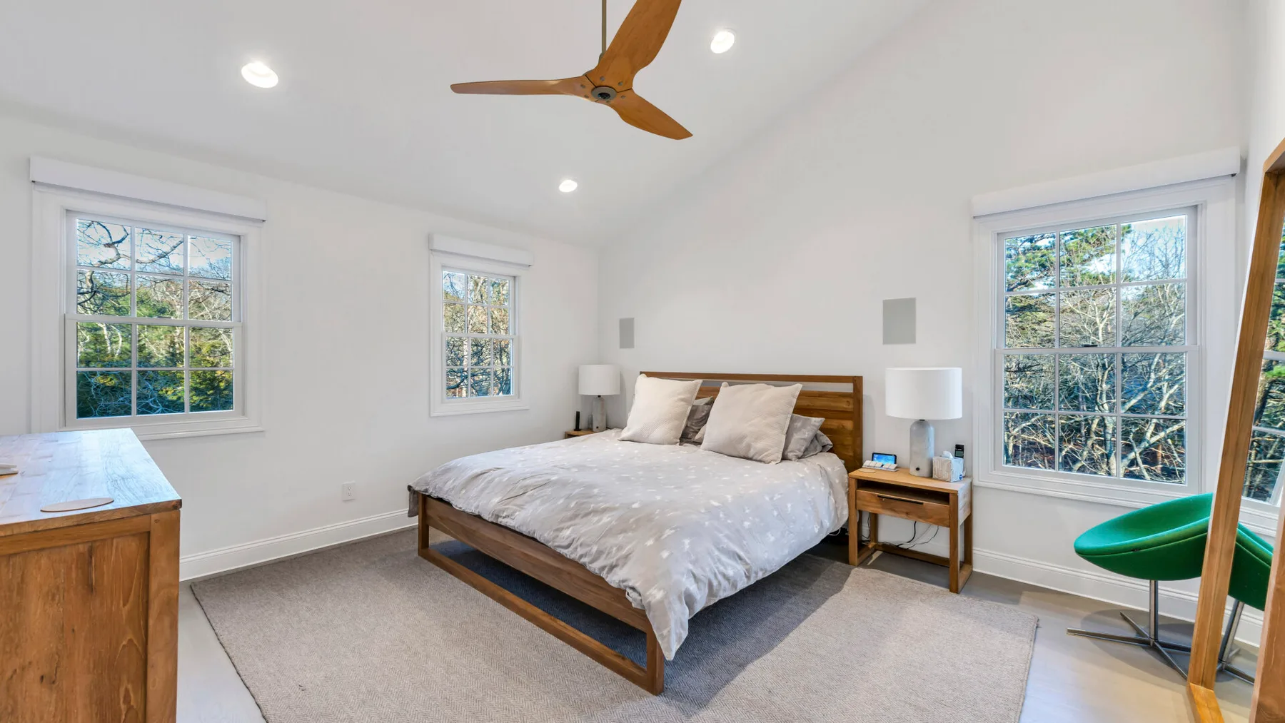 A bright bedroom with a wooden bed and windows overlooking greenery.