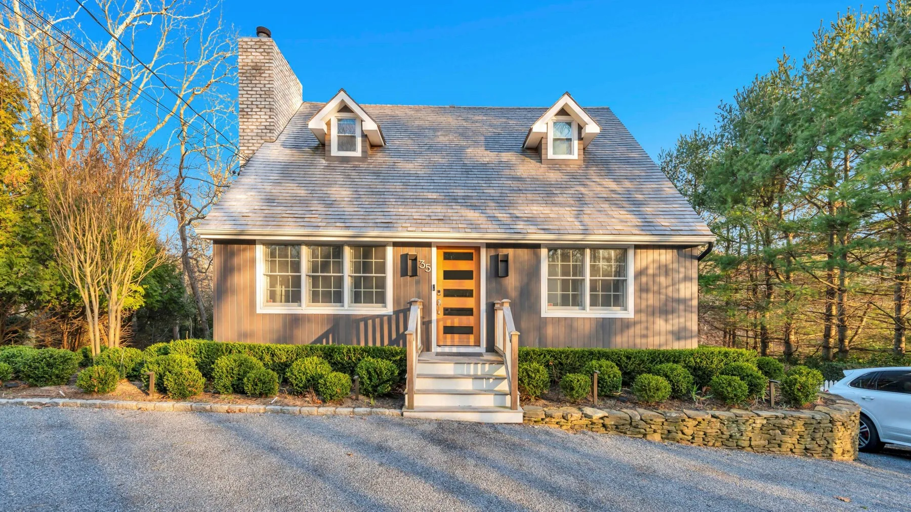 A cottage-style house faces a gravel driveway, with a centered front entrance.